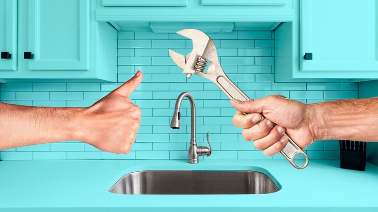 a hand with a thumbs up and another holding a wrench in front of a kitchen sink with blue tile and blue counter
