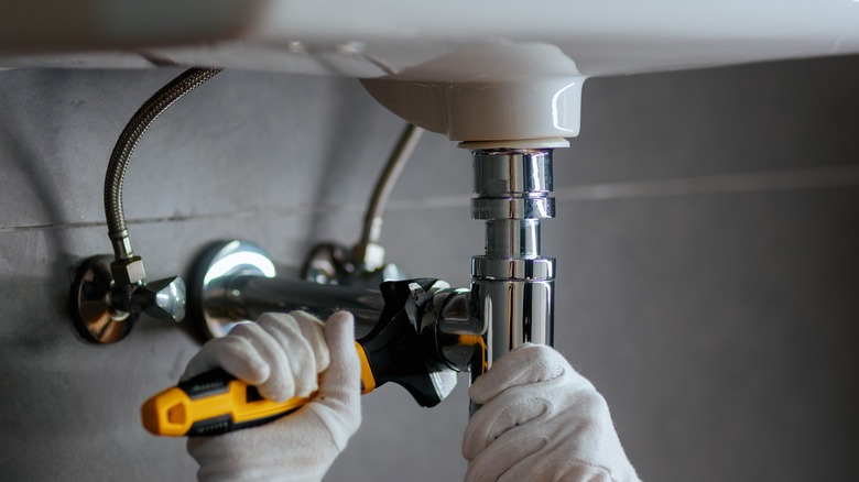 hands tightening plumbing lines from below