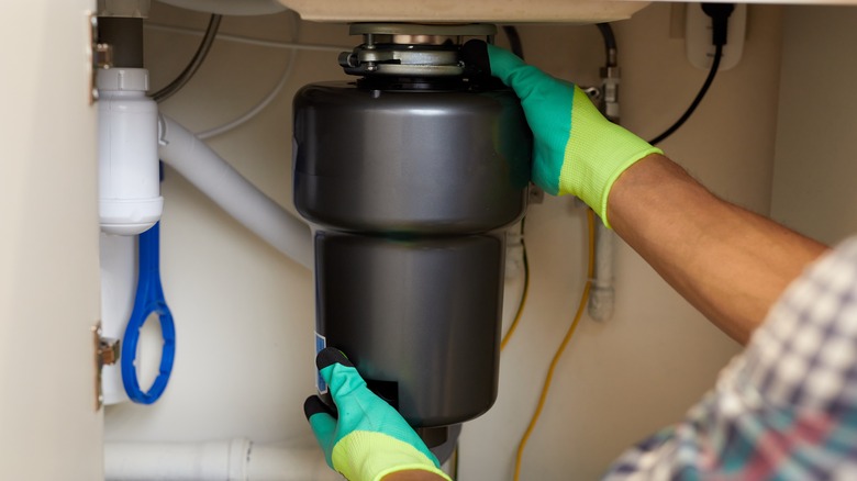 person holding garbage disposal under sink