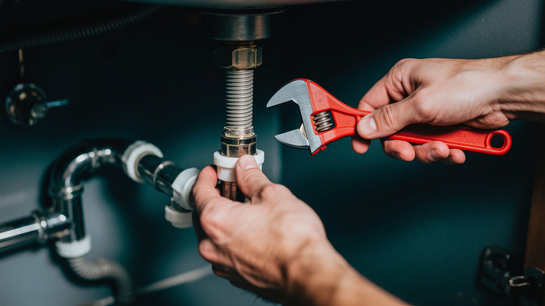hand holding wrench under sink