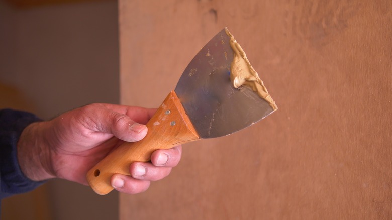 hand holding putty knife with putty on it
