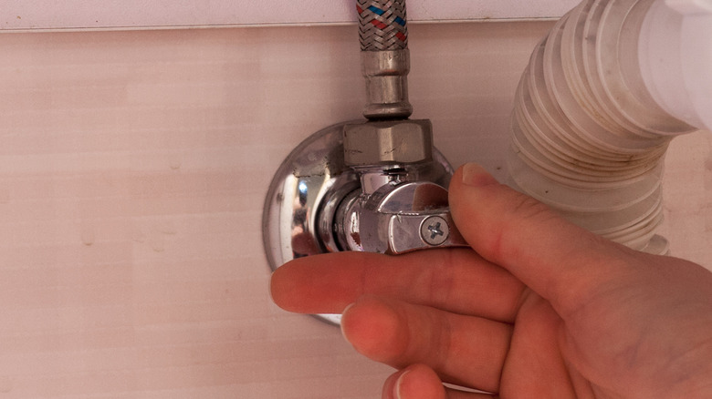 hand turning water shutoff valve under sink