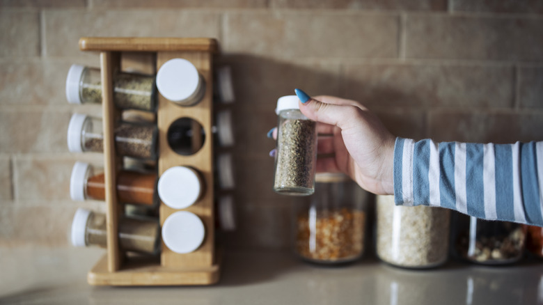 Cropped hand holding jar of spices on kitchen counter.