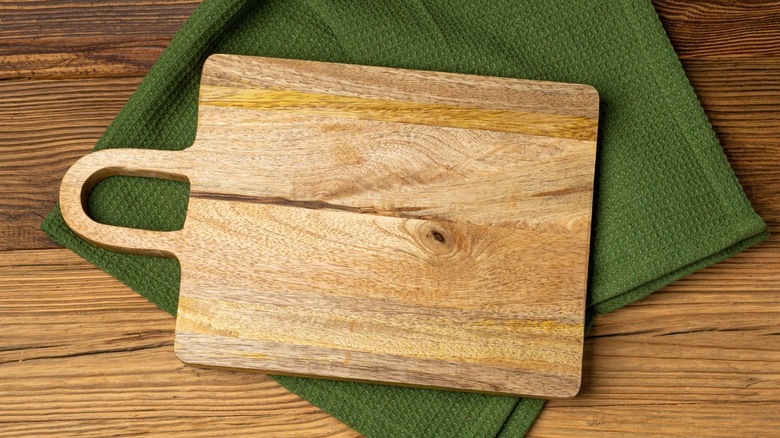 Wooden cutting board with green towels on table.