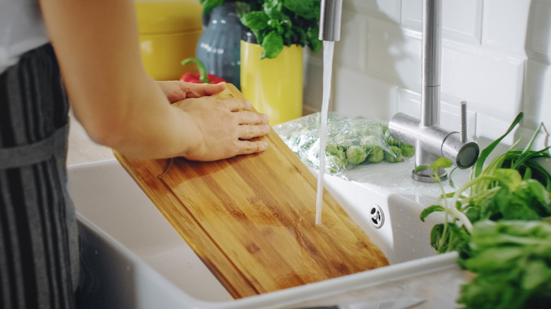 Wooden cutting board being washed in the sink.