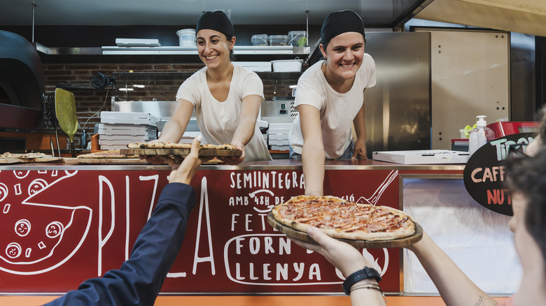 Two street vendors handing out whole pizzas