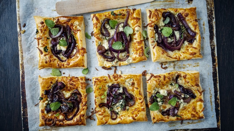 a sheet tray of red onion tarts with fresh herbs