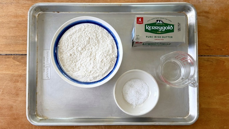 a sheet tray with a bowl of flour, salt, water, and a case of Kerrygold unsalted butter