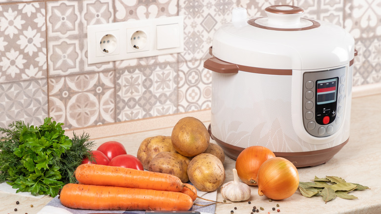 Slow cooker on a counter with raw vegetables