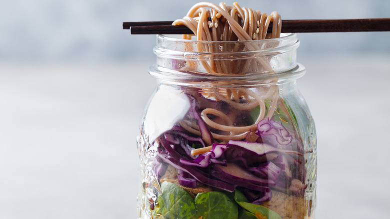 close-up of a mason jar noodle meal prep being eaten with chopsticks