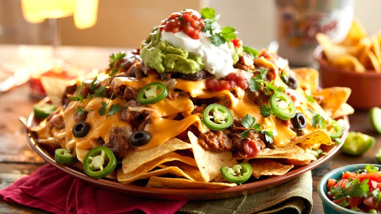 Plate of nachos covered in ground beef, cheese sauce, fresh jalapeños, sour cream, and salsa