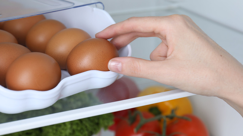 hand taking an egg from a ceramic container in a fridge