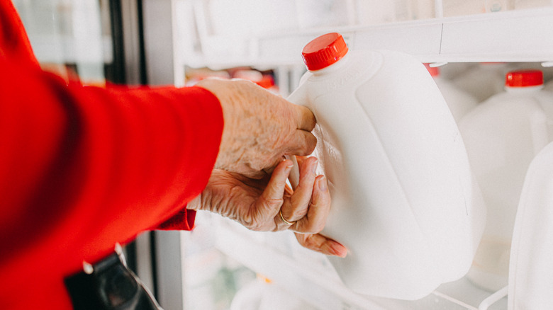 Elderly woman grabbing a gallon of milk from the fridge