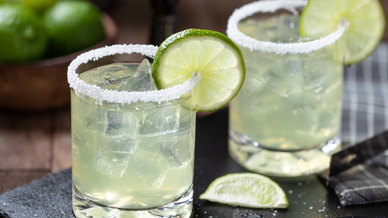 Two salt-rimmed margaritas in rocks glasses.