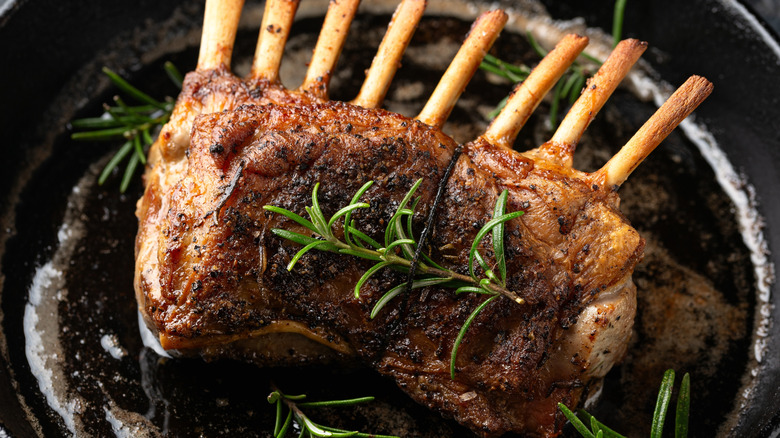A cooked rack of lamb with rosemary and butter in a cast iron pan