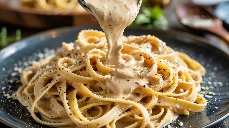 Pouring Alfredo sauce on fettuccine