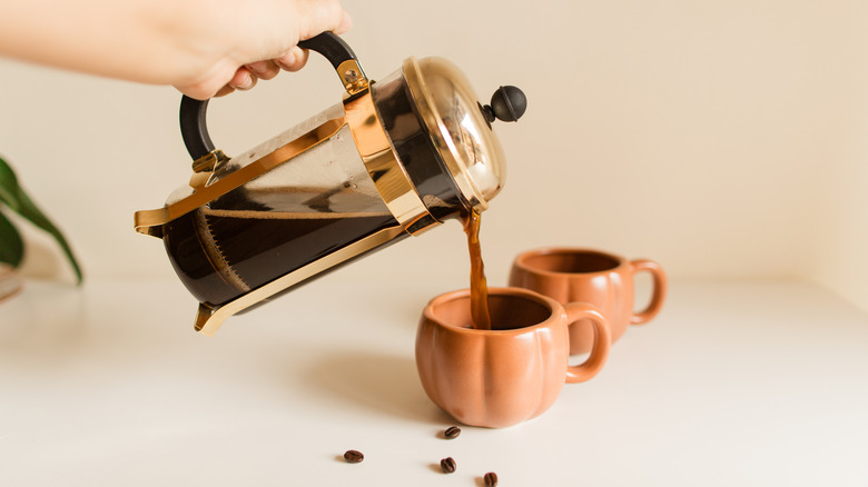 someone pouring coffee from a French press into cups