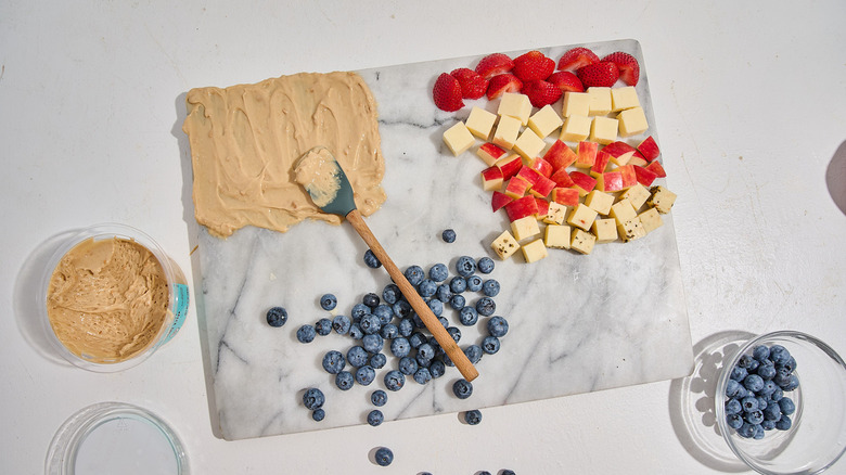 Snack board being built on a table with a spatula spreading the cannoli dip