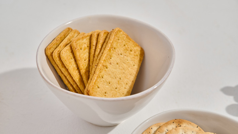 Crackers in a bowl on a table next to a snack board
