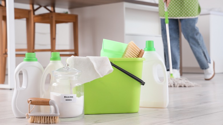 Someone mopping the floor in a kitchen with a range of cleaning products showcased.