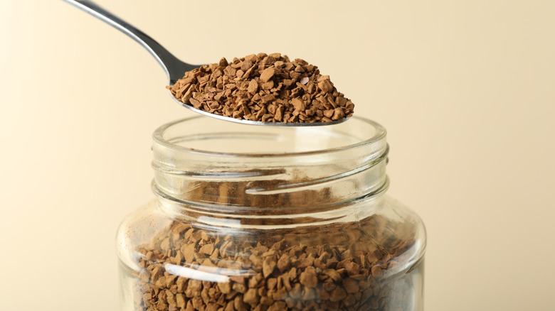 Spoon scooping out a spoonful of instant coffee from glass jar