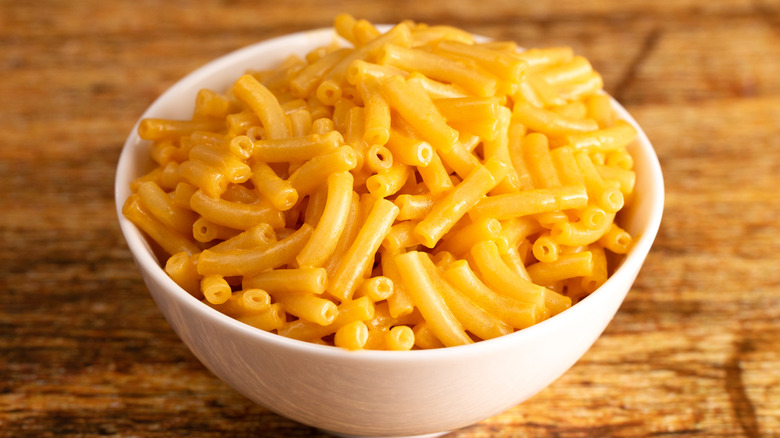 Boxed mac and cheese in a white bowl on a wooden table.