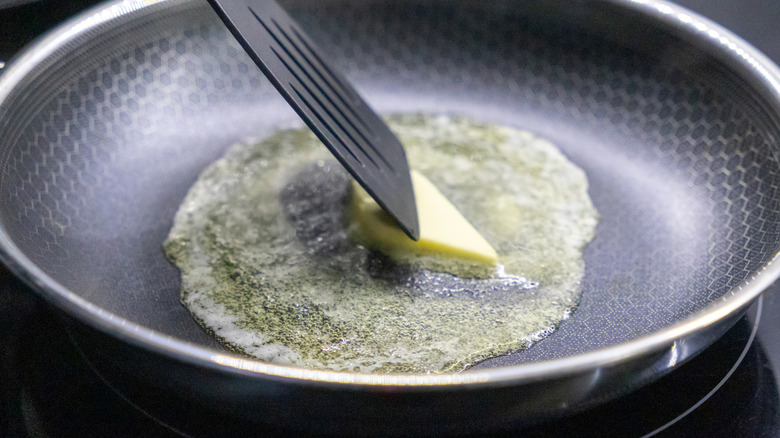 melting butter in a frying pan with a black spatula on a hot stovetop
