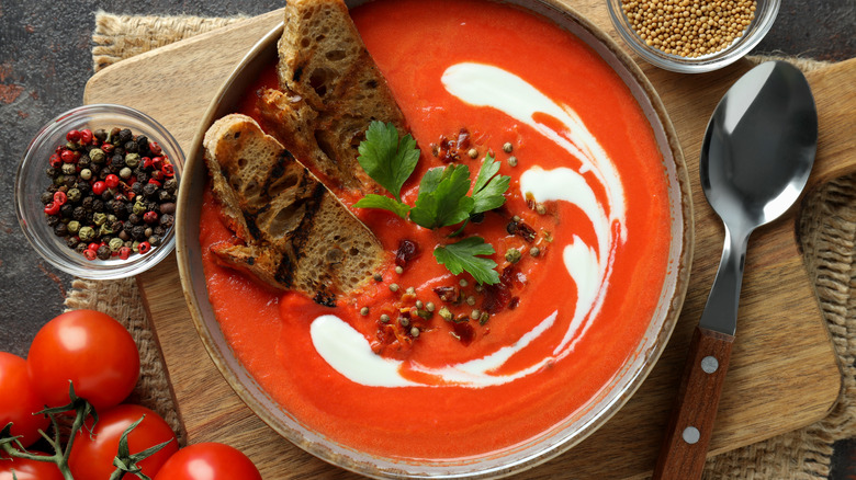 tomato soup with milk, croutons, and herbs on a wooden board