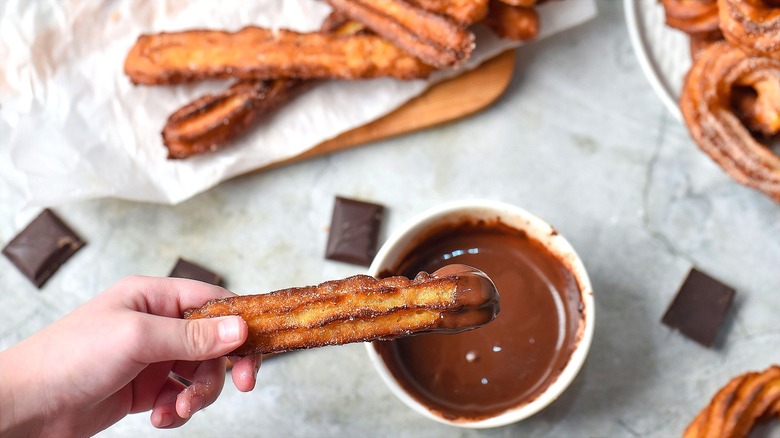 Hand dipping a golden brown churro in melted chocolate