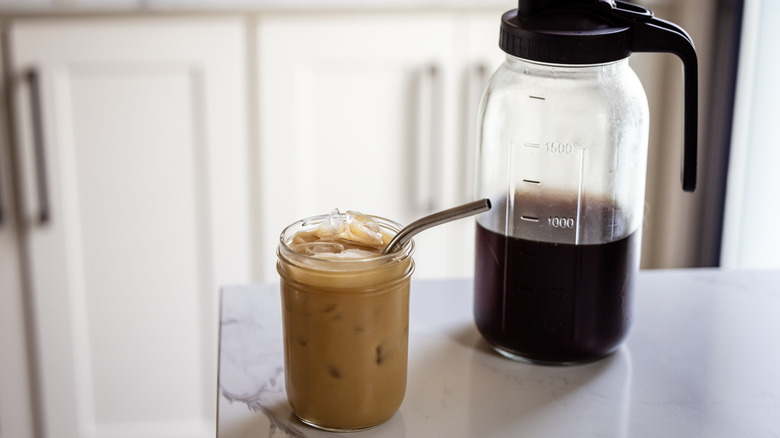 A pitcher half-full of cold brew and a latte in a cup with a straw