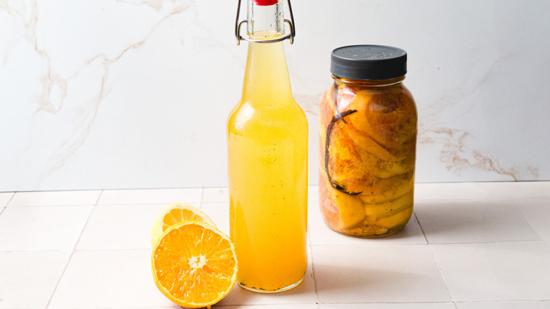 A bottle of citrus flavored vodka near jar and two citrus halves