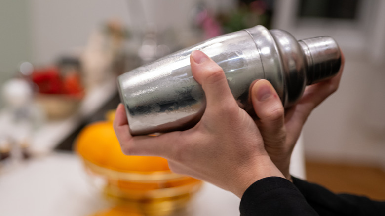A person's hands hold a cocktail shaker in motion.