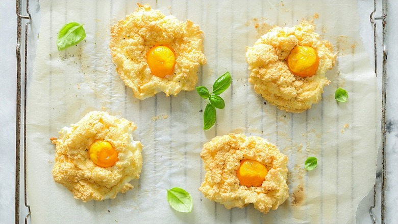 Baked cloud eggs on a parchment lined wire rack with basil leaves