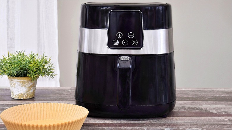 Black and silver air fryer with parchment paper liners on a white-washed wooden table