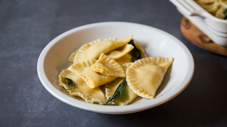 Pumpkin ravioli with butter sage sauce are served in a white dish on a gray table.