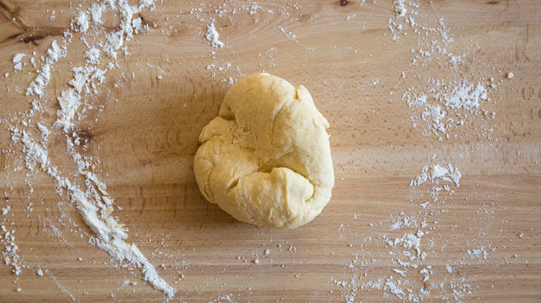 A partially kneaded ball of pasta dough sitting on a flour-sprinkled tabletop.