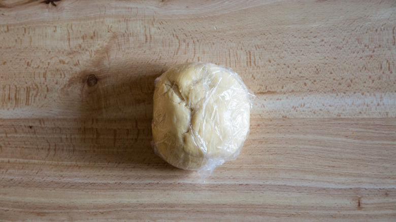 A plastic-wrapped ball of pasta dough sitting on a tabletop.
