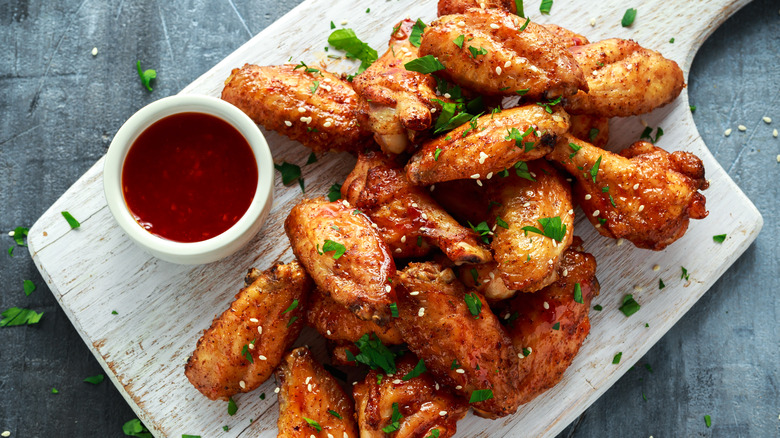 Baked chicken wings on a cutting board with chili sauce