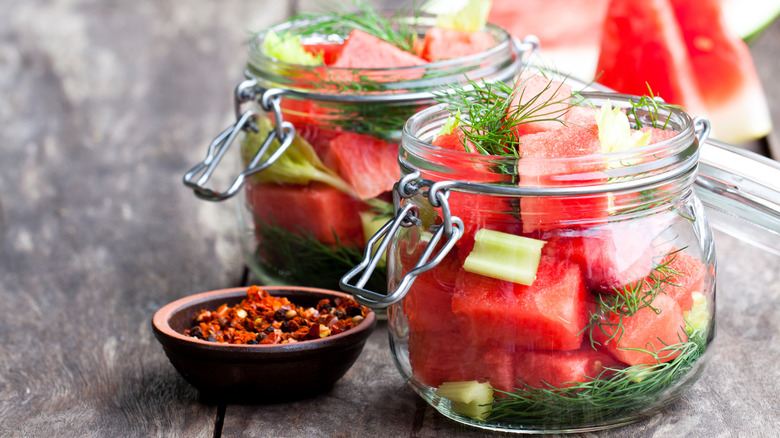 Marinated watermelon with herbs in a glass jar on wooden table