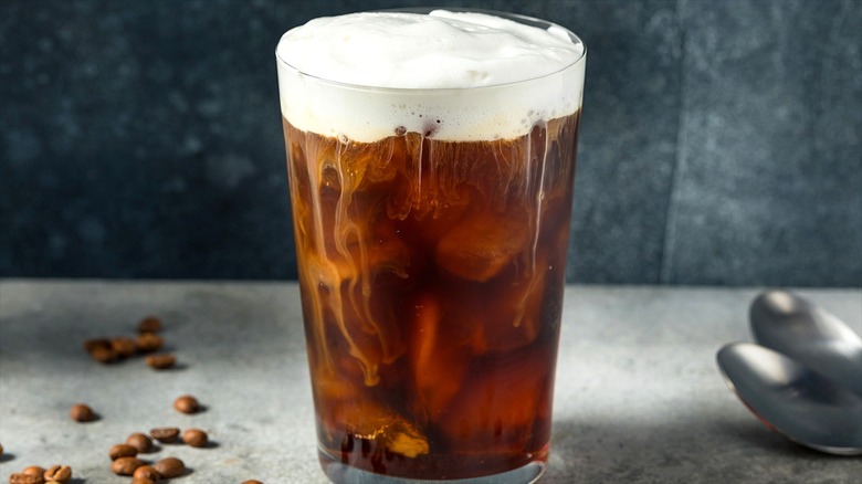 Clear tall glass of iced coffee topped with creamy cold foam