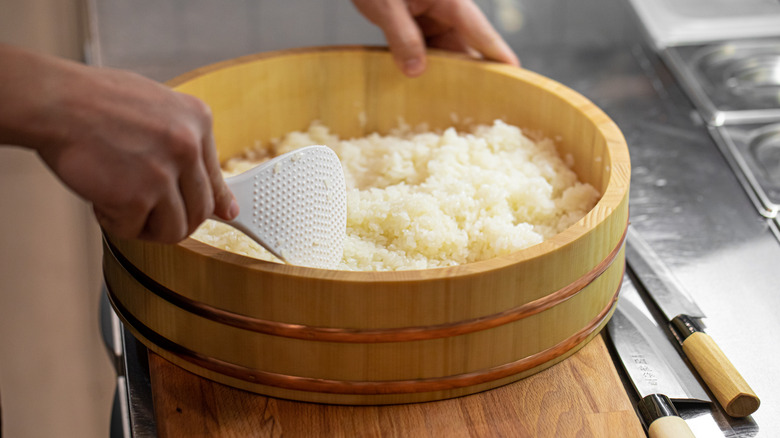 Chef mixing sushi rice in a hangiri bowl
