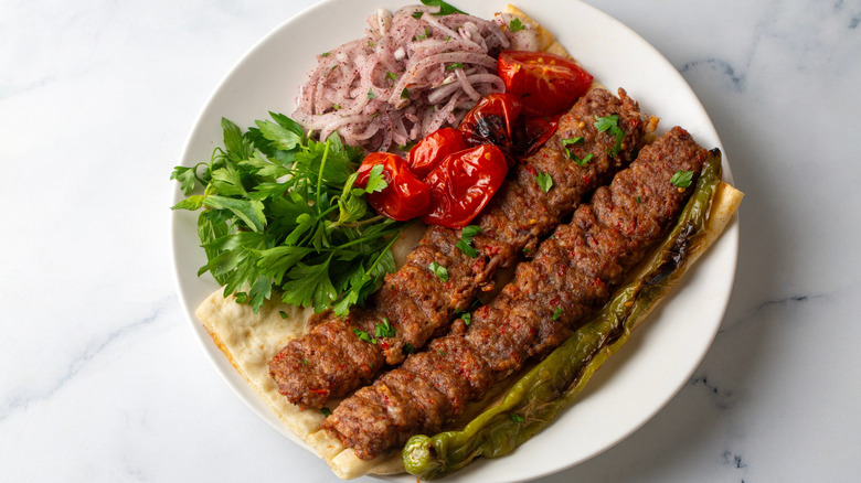 Two pieces of kebab meat on a flatbread with sides on a plate.