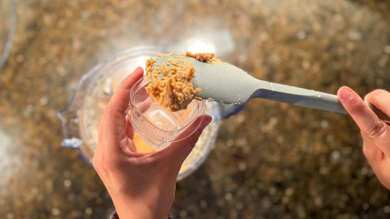 Person scraping peanut butter into a container