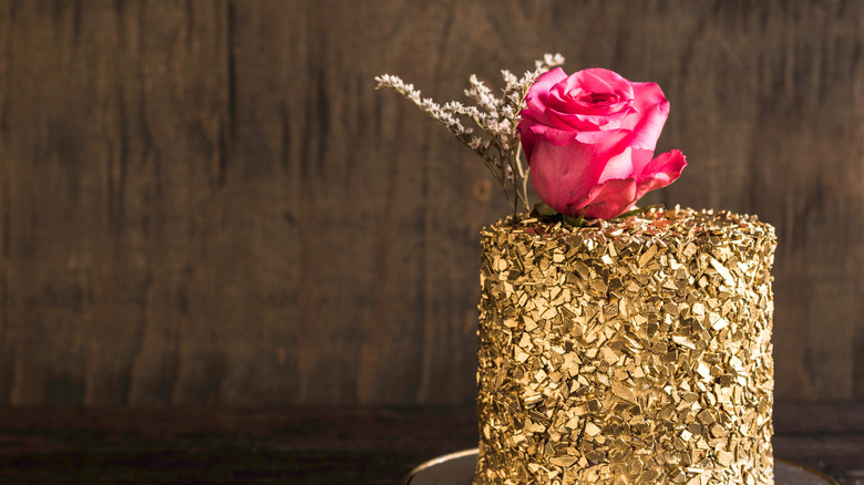 A cake has been decorated with gold flakes and a flower.