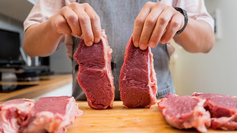 Hands holding up two raw steaks.