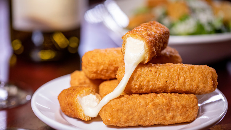 A plate of mozzarella sticks, with one sporting a satisfying cheese pull