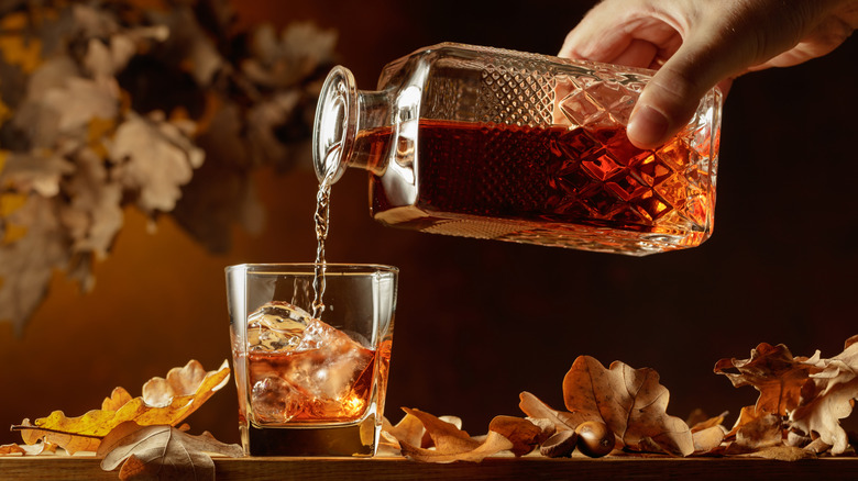 Whiskey being poured from a glass decanter into a glass with ice