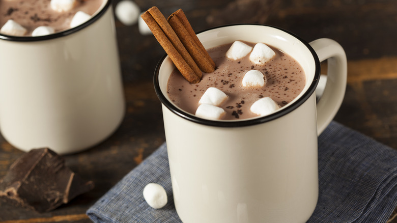 Hot chocolate with marshmallows and a cinnamon stick in a white mug