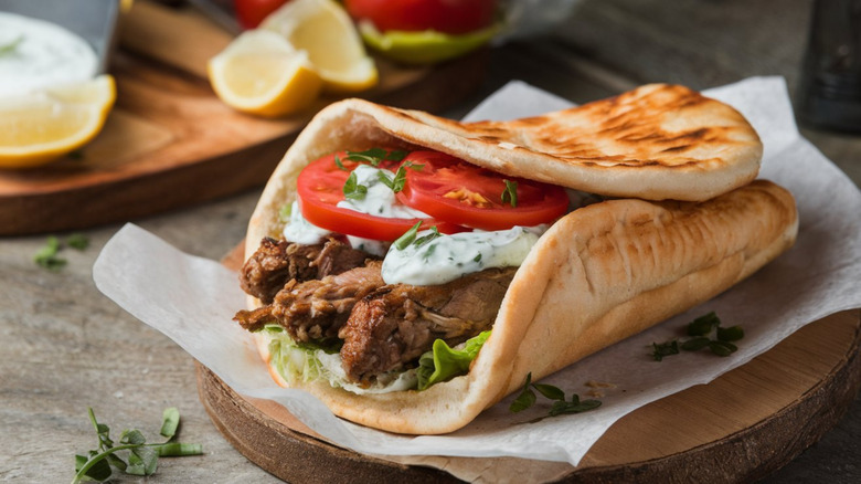 Greek gyro sandwich on parchment on round wood log-style plate.