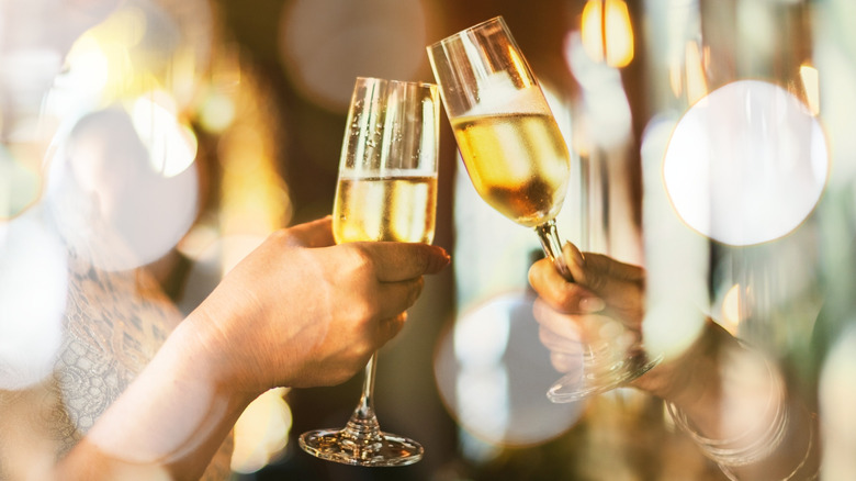 two hands clinking champagne glasses with bokeh background